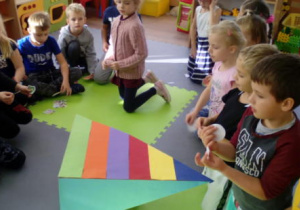 Przestrzenna kolorowa piramida ustawiona pośrodku siedzących w kole dzieci.